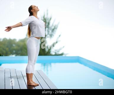 Sentendosi liberi in una giornata di sole. Scatto di una ragazza splendida che fa yoga all'aperto accanto a una piscina. Foto Stock