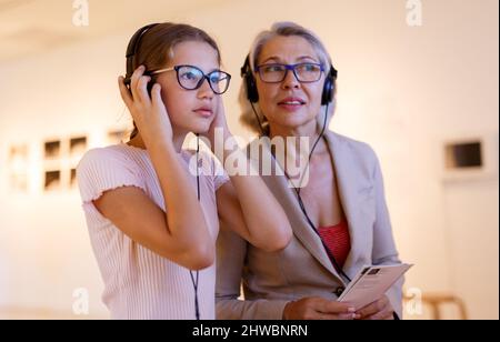 Attento tween ragazza con il senior donna esplorare art museum su auto-tour guidato Foto Stock