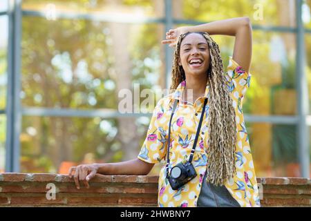 Donna nera con trecce africane, sollevando il braccio con gioia. Ragazza che tiene una macchina fotografica. Foto Stock