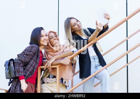 Eccitati giovani donne multietniche millennial sorridenti e prendere selfie su tablet Foto Stock
