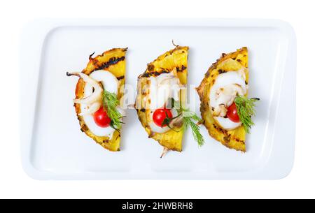 Immagine di seppia fritte su un grill con ananas, pomodorini e salsa Cile sulla piastra. Isolato su sfondo bianco Foto Stock