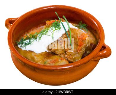 Gustosi rotoli di cavolo in foglie di cavolo in pentola di argilla con panna acida e verdure. Isolato su sfondo bianco. Foto Stock