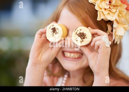 Aspetto dolce. Una bambina che tiene playfully i cupcakes davanti ai suoi occhi. Foto Stock