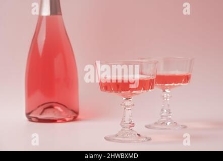 Due bicchieri di cristallo e una bottiglia di vino frizzante alle rose o champagne su sfondo rosa pastello. Concetto di vacanza. Composizione creativa minima con spazio di copia. Foto Stock