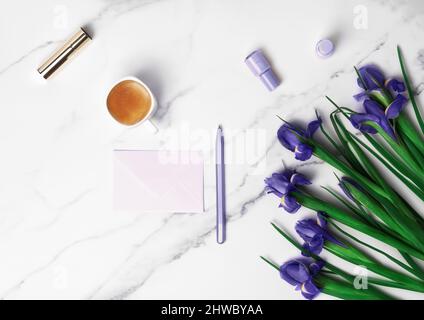 Tazza di caffè caldo del mattino, busta lilla con penna e belle iridi su sfondo di marmo. Disposizione piatta con spazio di copia per il testo. Biglietto di auguri per la Festa della Donna e il 8th marzo. Foto Stock