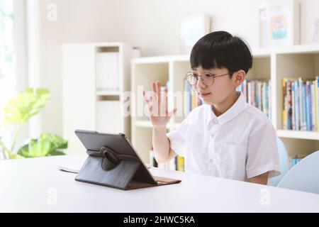 Ragazzo che studia via internet online con notebook e tablet, salutando insegnanti e amici, prendendo lezioni di video in rete a casa Foto Stock