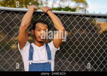 Uomo con le braccia sopra la testa appoggiate su una recinzione Foto Stock