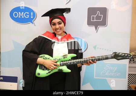 Una graziosa laureata asiatica si pone per una divertente fotografia alla sua cerimonia di laurea. Questo evento formale in cui le lauree (prima) cambiano in gradu Foto Stock