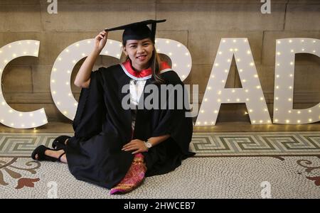 Una donna asiatica graziosa si pone per le fotografie alla sua cerimonia di laurea. Questo evento formale in cui le lauree (prima) si trasformano in laureati Foto Stock