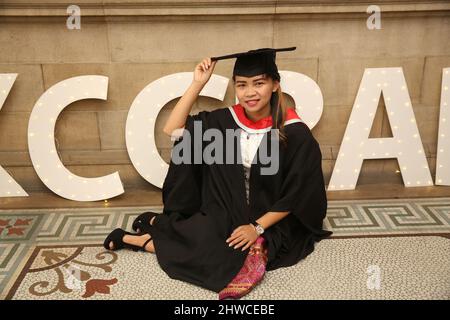 Una donna asiatica graziosa si pone per le fotografie alla sua cerimonia di laurea. Questo evento formale in cui le lauree (prima) si trasformano in laureati Foto Stock