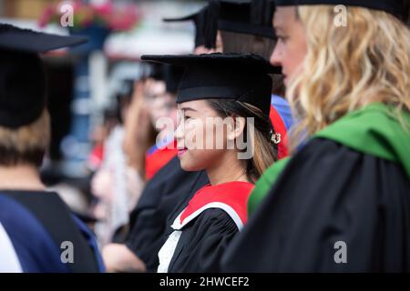 Una graziosa laureata asiatica si allinea con i suoi compagni laureati alla sua cerimonia di laurea. Questo evento formale in cui i diplomi (prima) cambiano Foto Stock