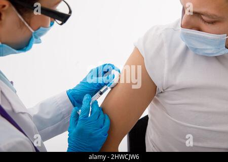 Il medico tiene una siringa prima di fare un'iniezione a un paziente in una maschera medica. Covid-19 o vaccino contro il coronavirus. Vaccinazione della popolazione Foto Stock