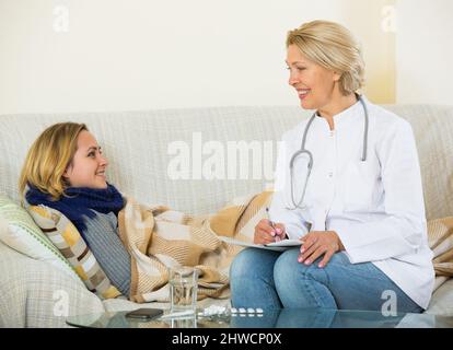 Giovane biondo con canna fumaria e febbre lamenta al terapeuta senior Foto Stock