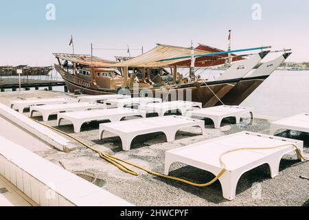 Ajman, UAE, Emirati Arabi Uniti - 26 maggio 2021: Dhow barca a vela vicino molo con sedie a sdraio nel giorno d'estate. Barca a vela ormeggiata vicino al molo della città, molo in Foto Stock