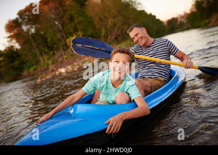 HES un piccolo ragazzo avventuroso. Sparato di un padre e di un figlio che remano una barca insieme su un lago. Foto Stock