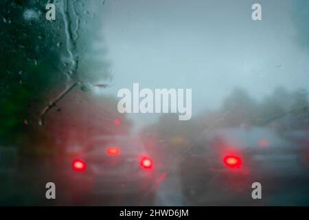 Immagine sfocata della retroilluminazione rossa delle auto. Immagine scattata attraverso gocce di pioggia che cadono su vetro bagnato, sfocature astratte del traffico - monsone immagine di riserva di Kolkata Foto Stock