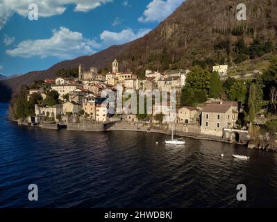 VISTA AEREA. Foto panoramica, vista da cartolina dal lago di un piccolo borgo antico in Lombardia, Lago di Como, Italia Foto Stock