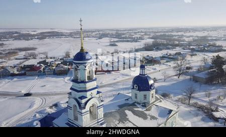 Vista ravvicinata sulle cupole blu e le croci dorate della chiesa ortodossa russa vicino al piccolo villaggio nella limpida giornata invernale. Religione e fede Foto Stock