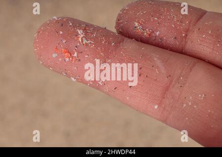 Il primo piano delle microplastica si trova sul dito dell'essere umano. Piccoli pellet di plastica a dito. Micro plastica, problema. Foto Stock