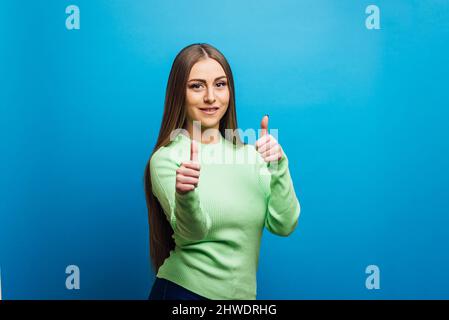 Giovane donna che mostra i pollici in su mentre si alza su uno sfondo isolato. Foto Stock