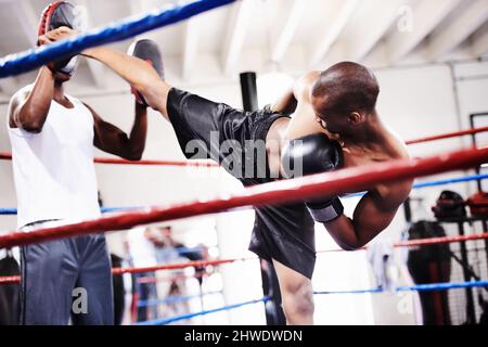 Lanciare un magnifico calcio. Un kickboxer che lancia un calcio forte ai suoi guanti sparring partner. Foto Stock