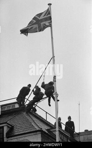 Due uomini in kit di alpinisti hanno salito il flagpole in cima alla casa di Rhodesia a mezzanotte il 11th gennaio: Hanno preso la bandiera del Rhodesia, la hanno sostituita con l'Union Jack e hanno detto agli agenti di polizia che hanno cercato di abbattere, Che erano stati messi fino alla manifestazione pomeridiana il 12th gennaio fuori Rhodesia House. Alle 10am avevano dei panini mentre erano ancora sul flagpole e poi uno di loro leggeva un libro. 12th gennaio 1969. Foto Stock