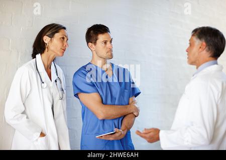 Theyre nel commercio di salvare le vite. Un taglio corto di tre medici in piedi e di avere una conversazione seria. Foto Stock