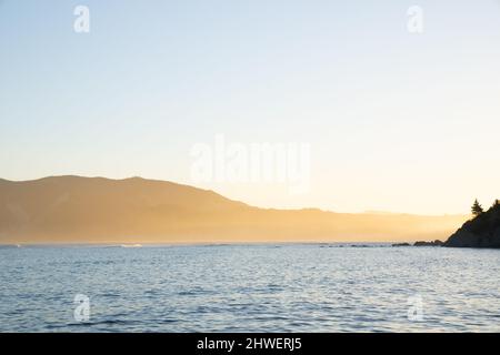 Ammira la baia di Tokomaru nel tardo pomeriggio mentre il sole illumina le colline lontane in un bagliore dorato sopra il mare. Foto Stock