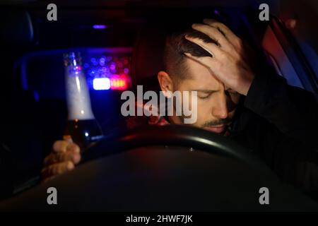 Polizia stradale con luci lampeggianti ferma ubriaco conducente. Giovane uomo che beve birra mentre guida l'auto. Conducente sotto l'influenza dell'alcol Foto Stock