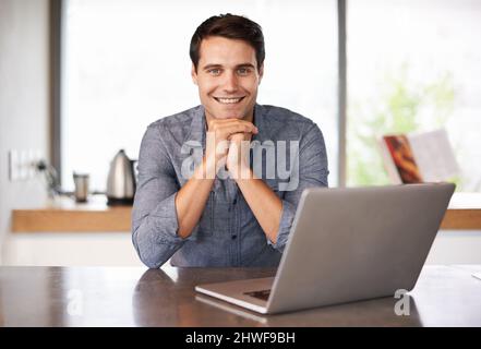 Trascorrendo un po' di tempo di qualità con il suo notebook. Ritratto di un bel giovanotto seduto in cucina con il suo laptop. Foto Stock