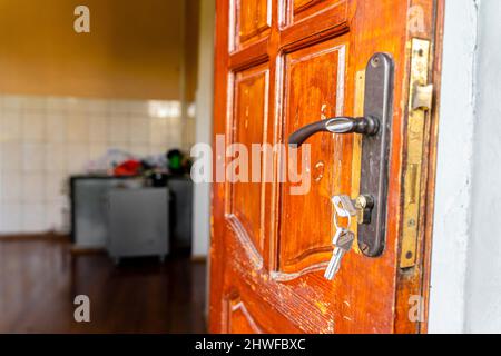 Le chiavi nella serratura e la maniglia della porta sulla vecchia porta di legno aperta Foto Stock