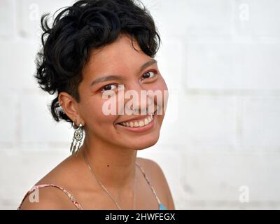 Giovane positivo ottimista bella fresca messicana Latina donna con capelli corti ricci e piercing naso sorride per lo spettatore. Foto Stock