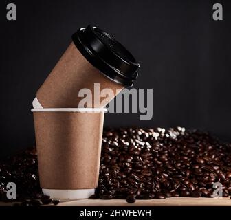 Rimanere a terra, dare calore e condividere un latte amore. Primo piano di due tazze di carta con chicchi di caffè sullo sfondo. Foto Stock