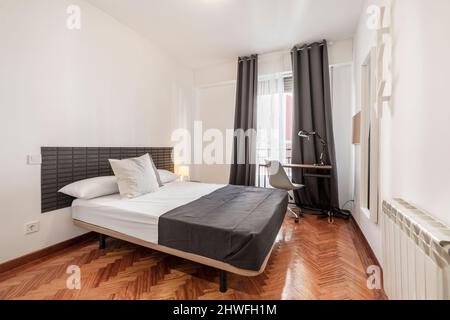 Camera da letto con letto king size, scrivania con lampada e pavimento in parquet a spina di pesce Foto Stock