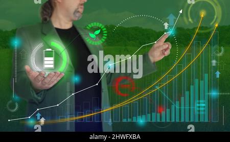 Uomo d'affari disegna il grafico di crescita e tiene il segno della batteria con le foglie verdi - concetto di energia verde Foto Stock