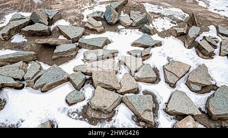 Grandi rocce e pietre raccolte in una cava di roccia con neve che si scioglie sui lati che saranno utilizzati per paesaggio paesaggistico. Foto Stock