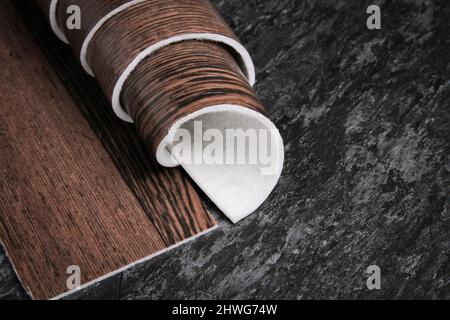 Linoleum. Rotolo di linoleum su sfondo nero. Rivestimenti per pavimenti. Posa di rivestimenti per pavimenti. Tessitura di legno su un rotolo. Il campione viene arrotolato. Foto Stock