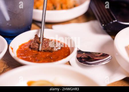 Barbecue coreano alla griglia per mangiare. Affettato di maiale utilizzando chopstick immersione in salsa piccante barbecue giapponese stile cibo, tradizionale coreano chiamato Yakiniku Foto Stock