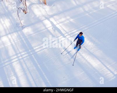 L'atleta uomo allena lo sci di fondo in inverno su una pista coperta di neve nella foresta. Foto Stock