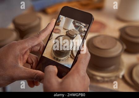 Ceramista fotografando i suoi prodotti di terracotta in studio di ceramica Foto Stock