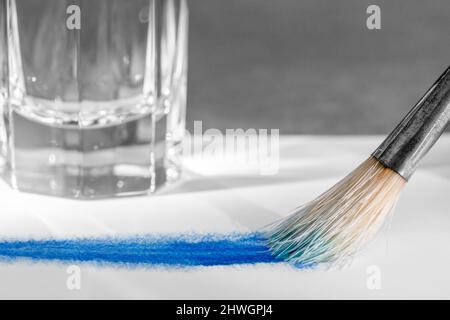 Arte e tema artigianale che mostra una punta di pennello e tintura di fronte a un bicchiere d'acqua Foto Stock