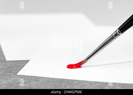 Arte e tema artigianale che mostra una punta di pennello con vernice rossa su fogli di carta bianca Foto Stock