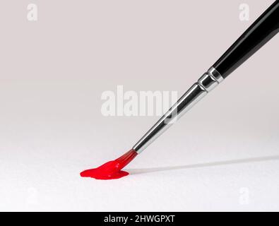 Arte e tema artigianale che mostra una punta di pennello con vernice rossa su carta macinata Foto Stock