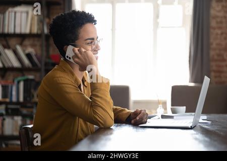 Allegro dipendente dell'ufficio africano in occhiali che risponde alla chiamata telefonica Foto Stock