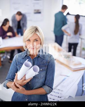 Ha grandi progetti per il futuro. Ritratto di una donna matura architetto in piedi in un ufficio con progetti. Foto Stock