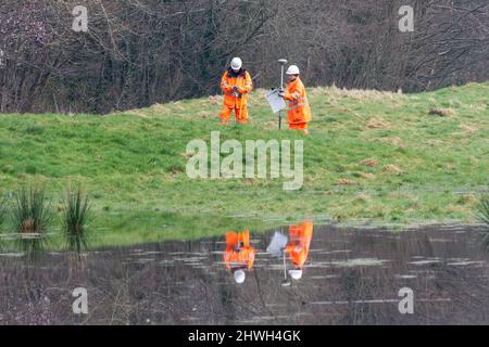 Due operai in abbigliamento ad alta visibilità che esaminano la portata e la causa di inondazioni in un parco di campagna, Hampshire, Inghilterra, Regno Unito Foto Stock