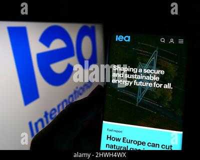 Persona che tiene il cellulare con il sito web dell'organizzazione Agenzia Internazionale dell'energia (IEA) sullo schermo con il logo. Concentrarsi sul centro del display del telefono. Foto Stock
