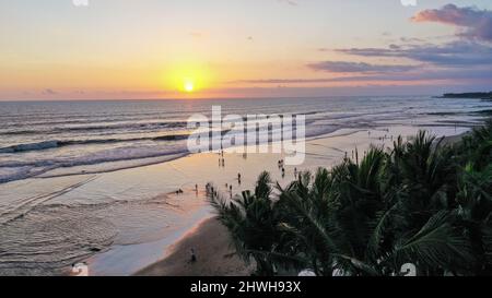 Le persone camminano lungo Echo Beach prima del tramonto. Scatto aereo di turisti godere del tempo prima del tramonto alla spiaggia popolare a Canggu sull'isola tropicale di Foto Stock