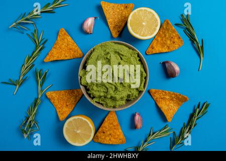 Composizione di guacamole con gli ingredienti per la sua creazione e il nachos per il suo consumo su sfondo blu Foto Stock