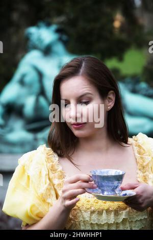 ritratto di giovane donna all'aperto in abito storico giallo che tiene la tazza Foto Stock